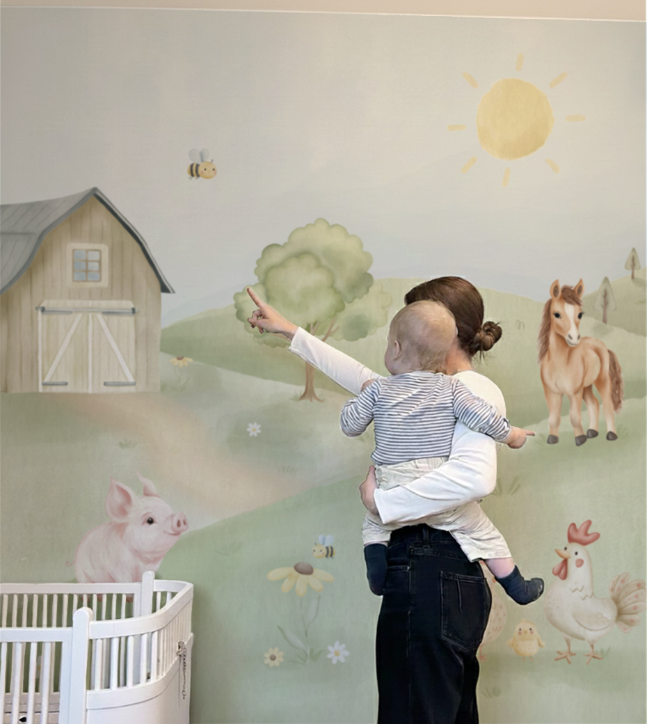 Mãe e bebê interagindo com o papel de parede Animais da Fazendinha em aquarela, apontando para a abelha. Quarto infantil com berço branco.